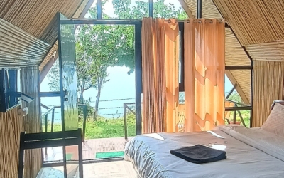 Cabin interior with bamboo walls, large bed, and glass door access to a balcony with an outdoor view.